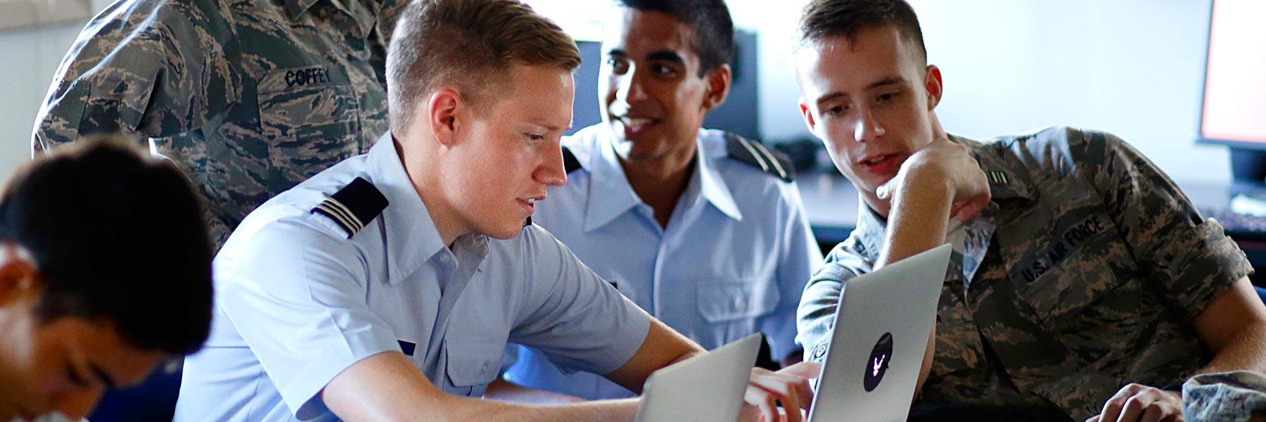 Cadets gather around a laptop during a study session.
