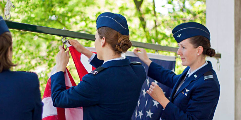 Female cadets in dress blues raise a U.S. flag.