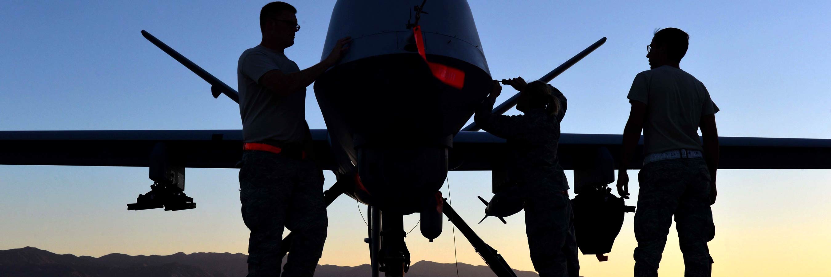 The silhouettes of two airmen with a fighter jet on a tarmac at sunrise